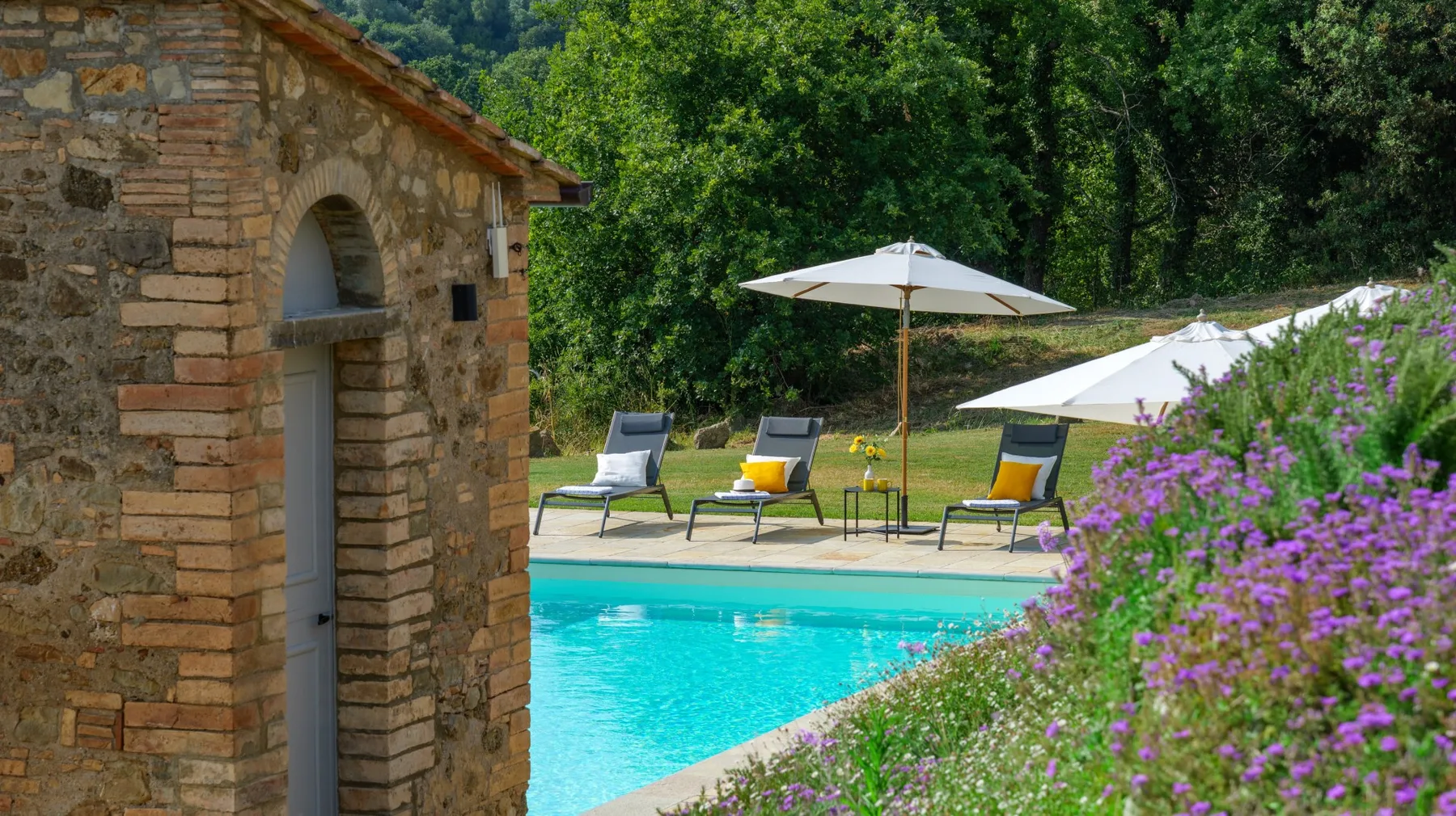 An outdoor swimming pool beside a stone building, with loungers and parasols.