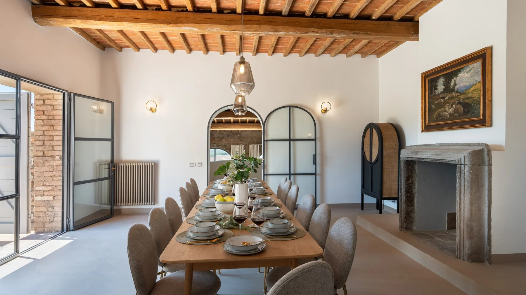 A dining room with a long table set for a meal beneath exposed wooden ceiling beams.