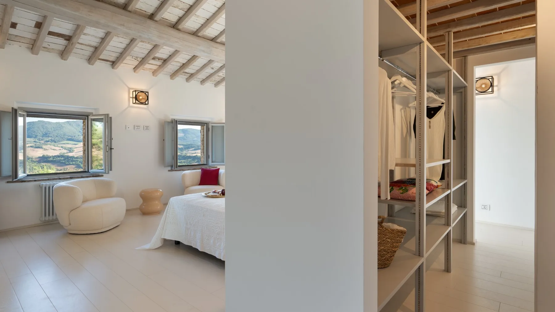 A bright bedroom with a bed, open windows, and an adjoining clothes-storage area.