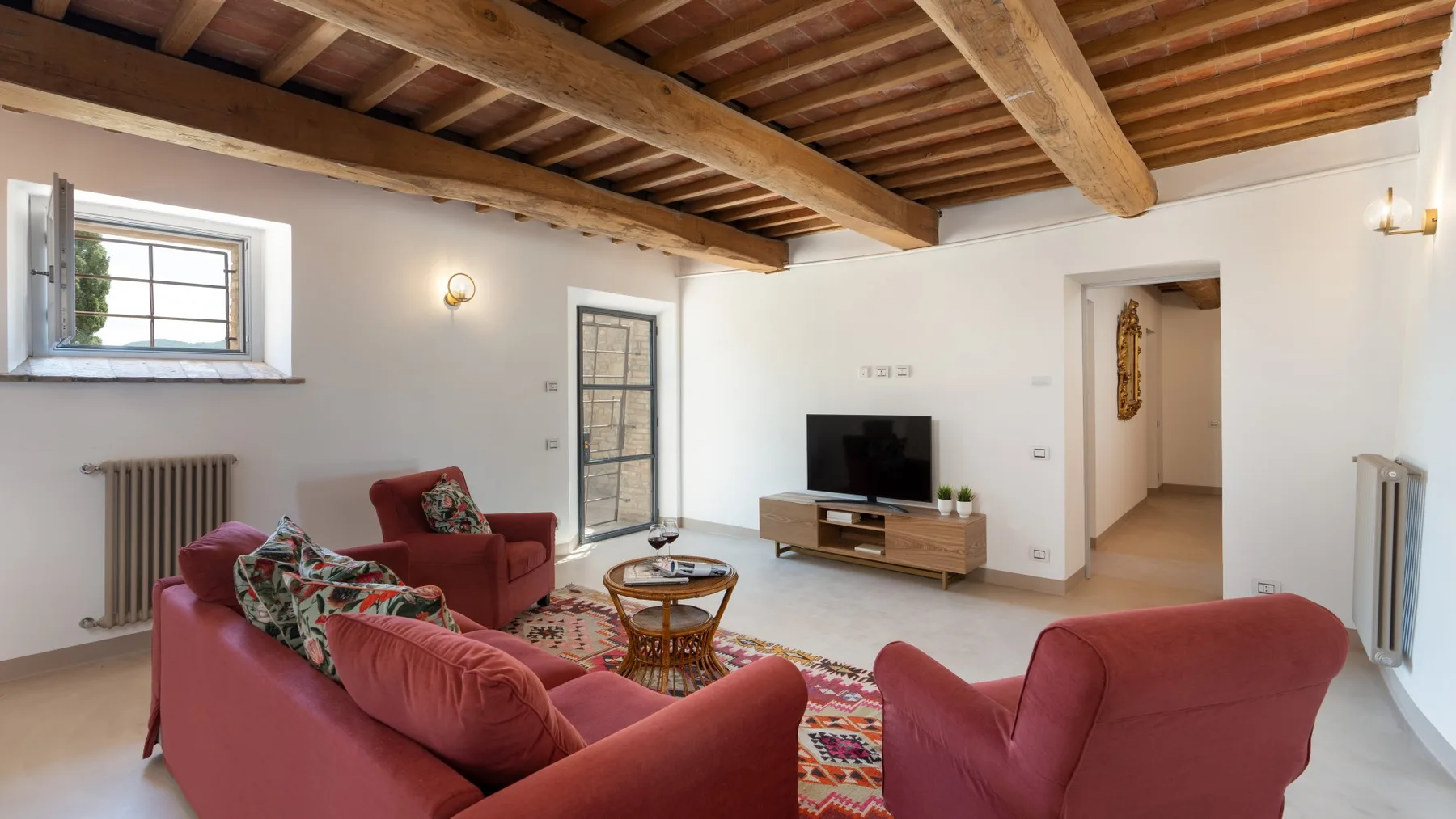 A living room with red seating, a television, and exposed wooden ceiling beams.
