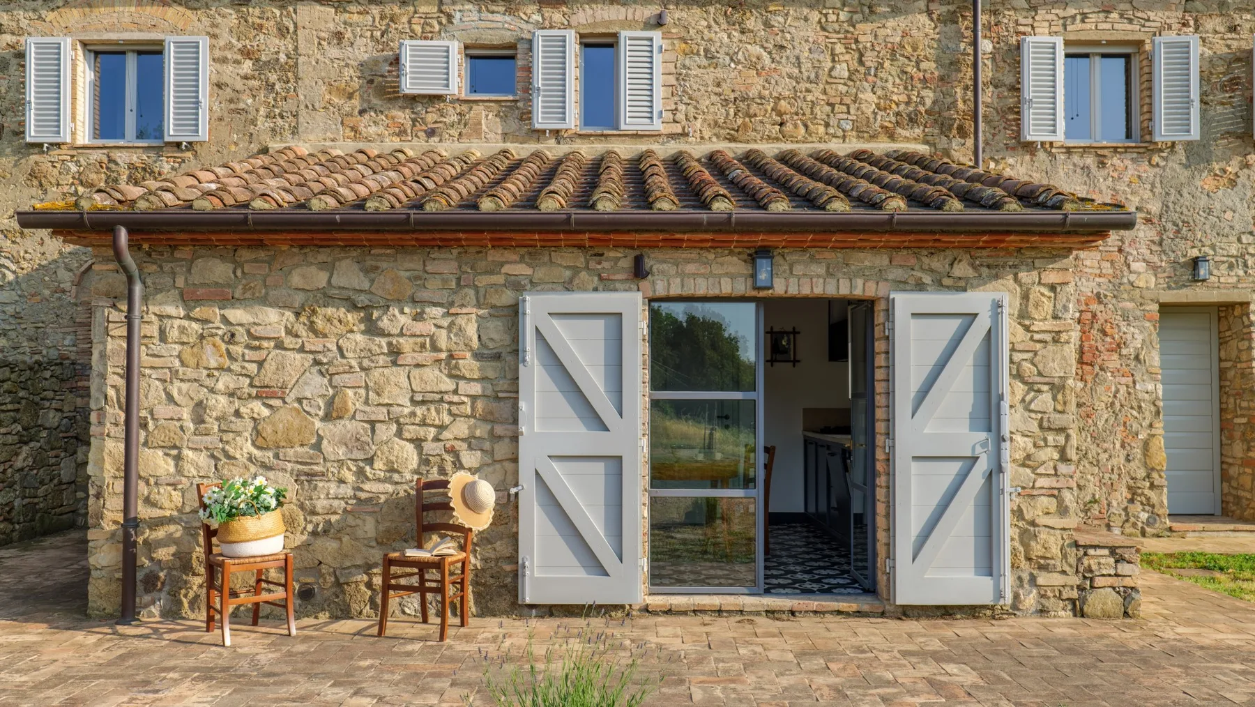 A stone building facade with pale shutters around an open doorway.