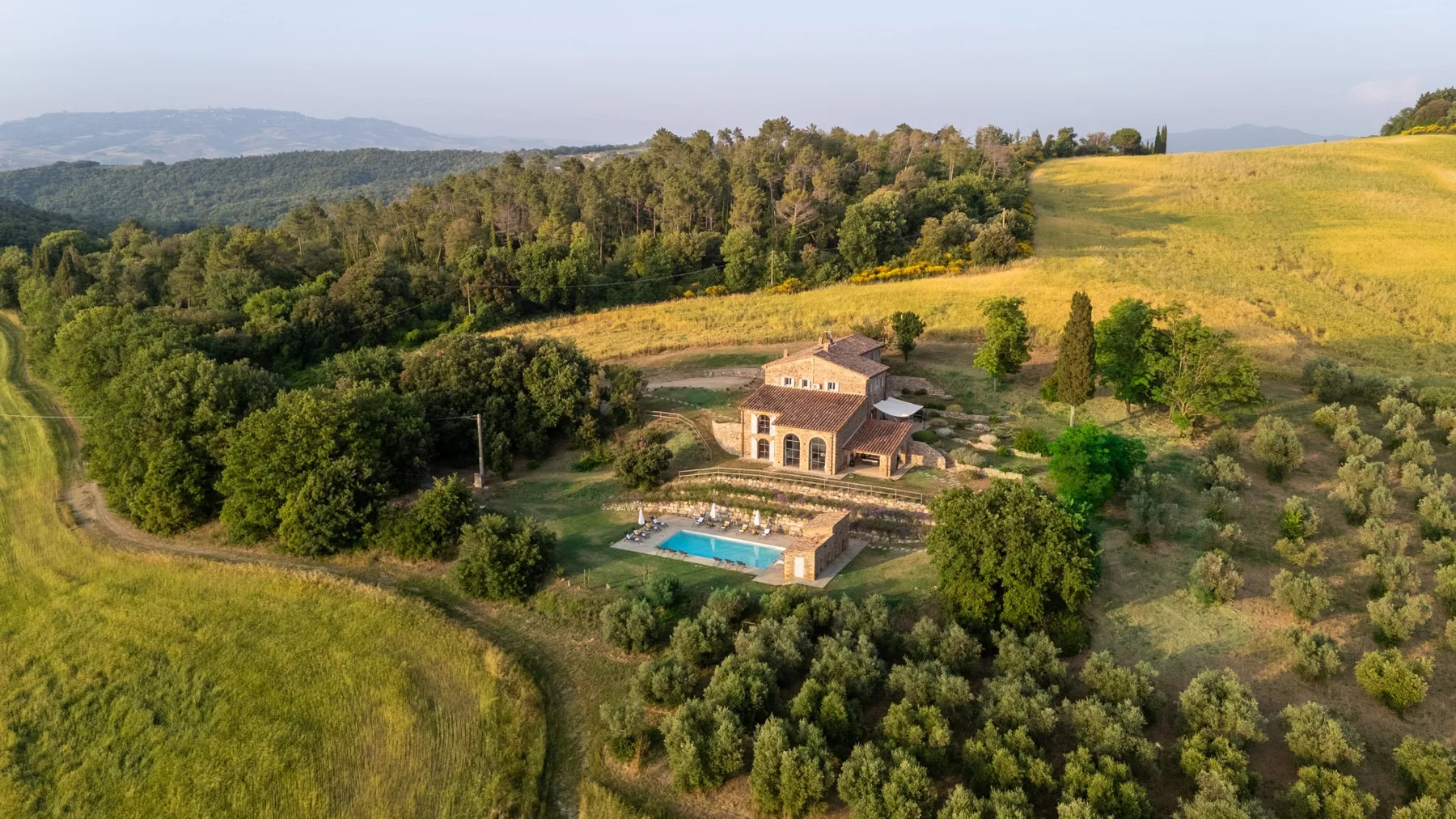 An aerial view of a countryside property with a swimming pool amid rolling fields and trees.