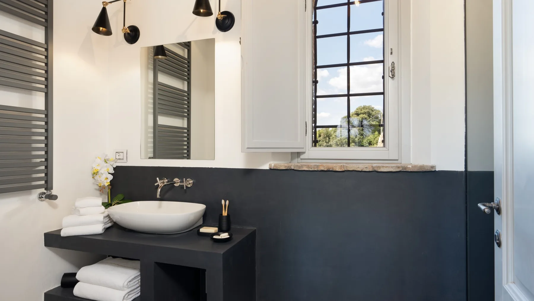 A bathroom vanity with a white basin, dark counter, and window above.