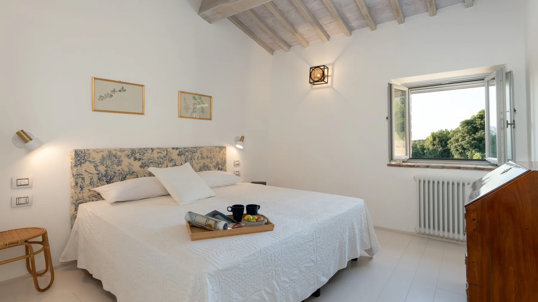 A bright bedroom with a large bed, framed pictures, and an open window.