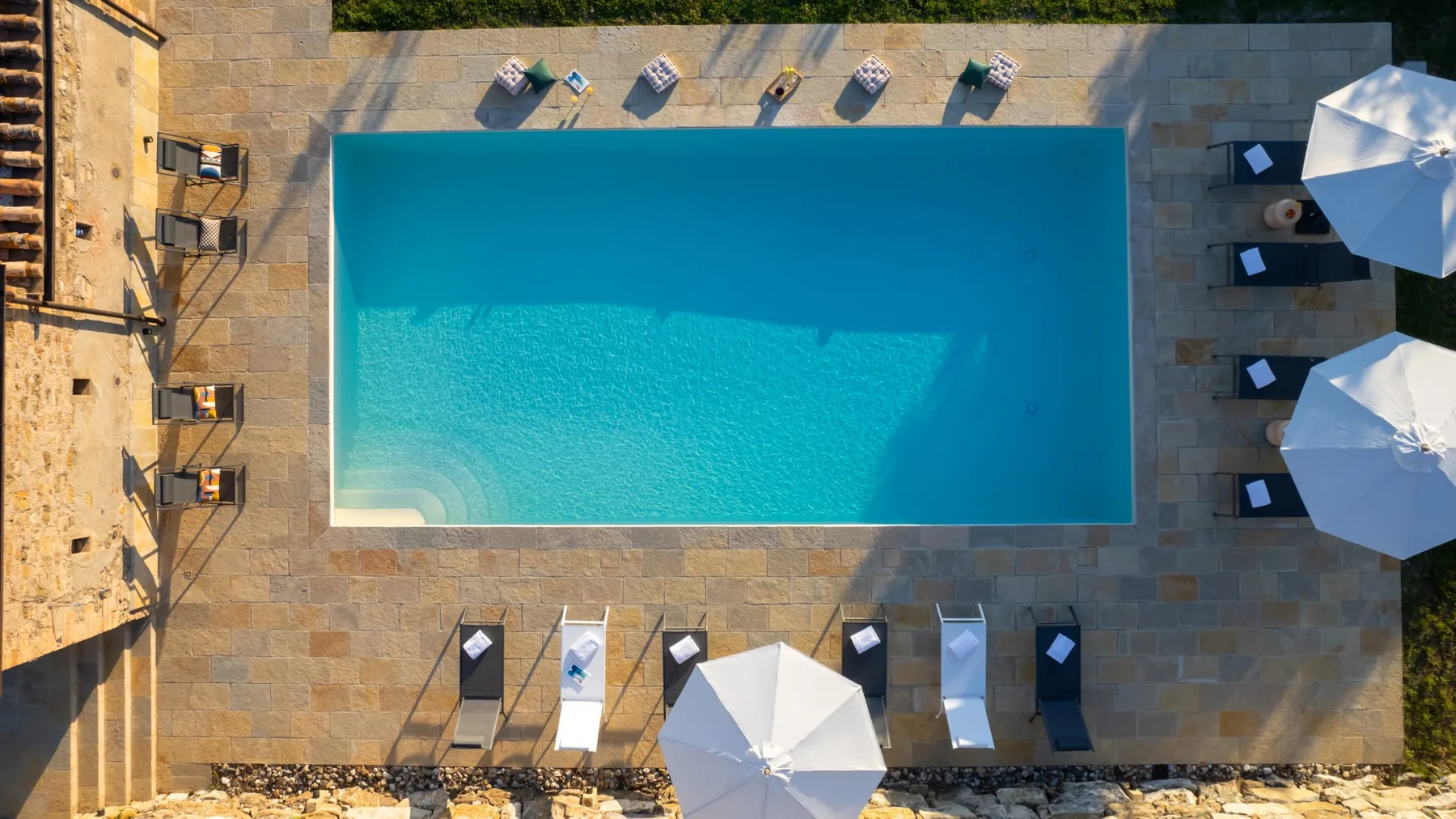An outdoor swimming pool is surrounded by a paved deck with loungers and umbrellas.