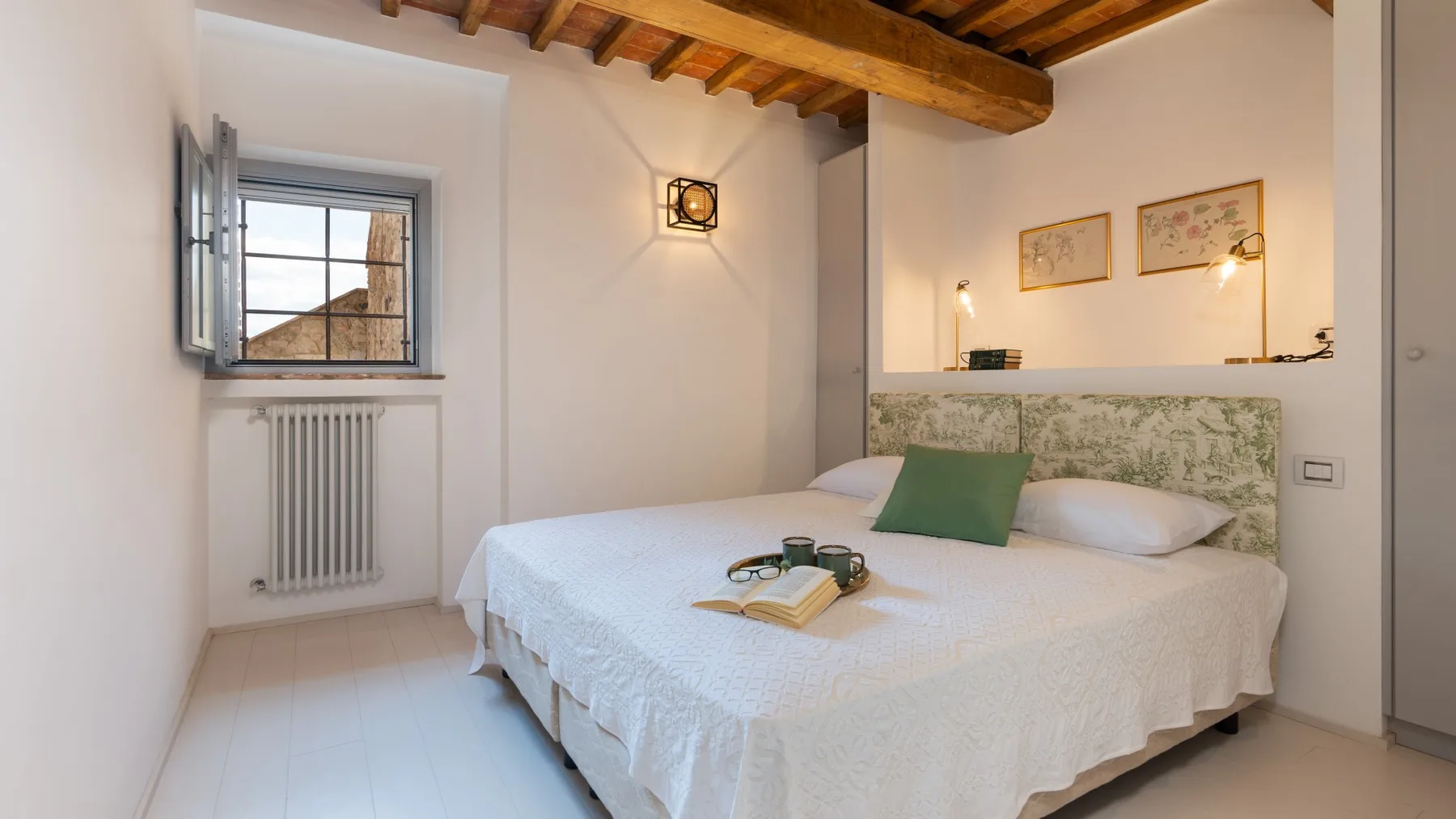 A bedroom with a bed, window, and exposed wooden ceiling beams.