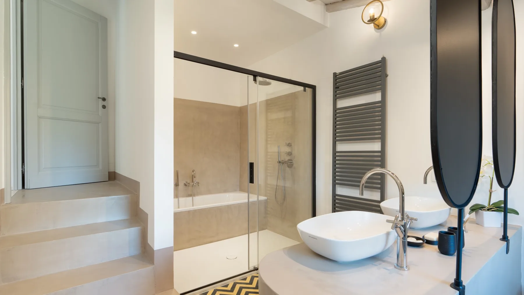 A modern bathroom with a glass shower, vessel sink, and wall-mounted towel radiator.