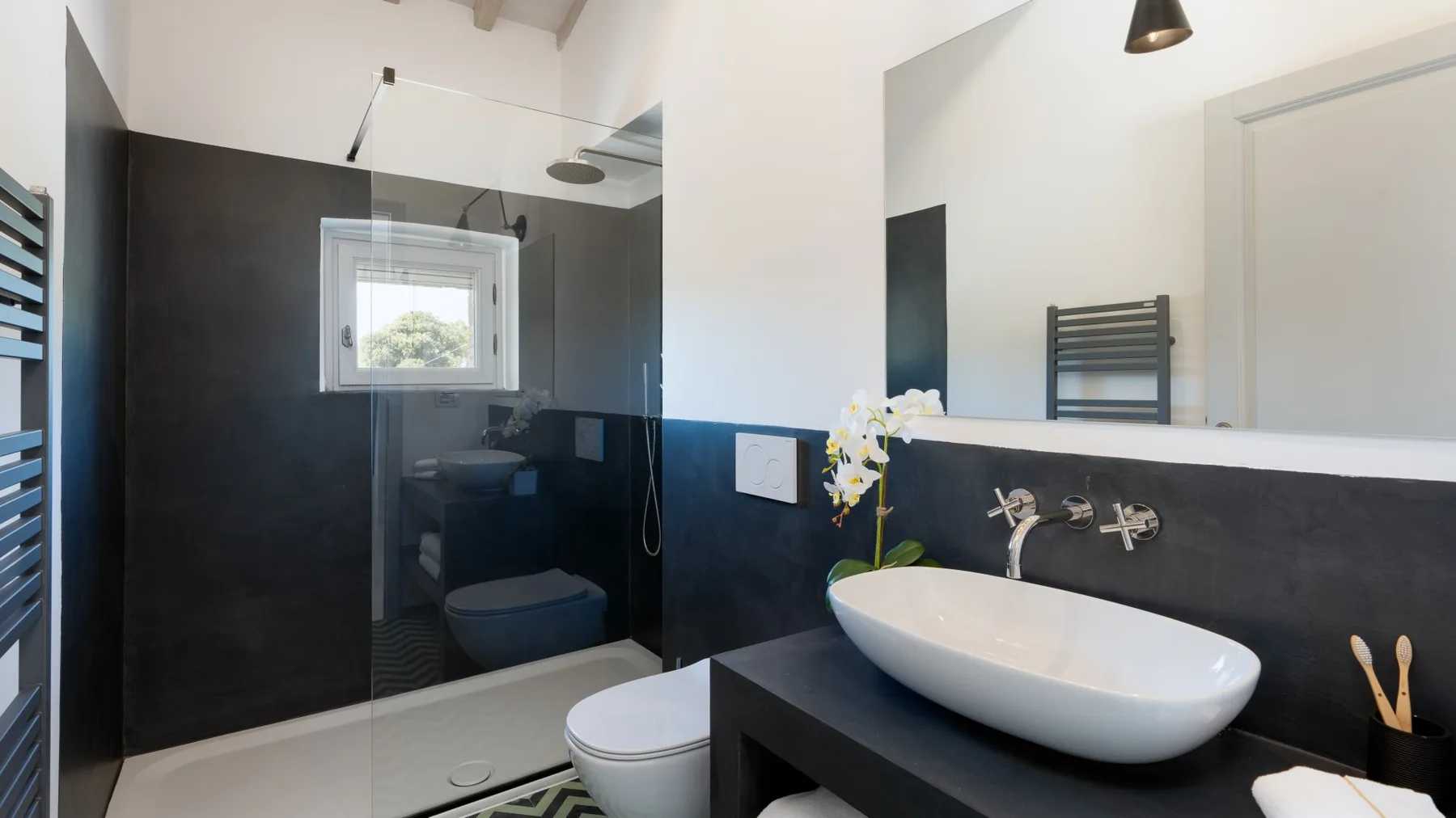 A modern bathroom with a white vessel sink and dark wall tiles.
