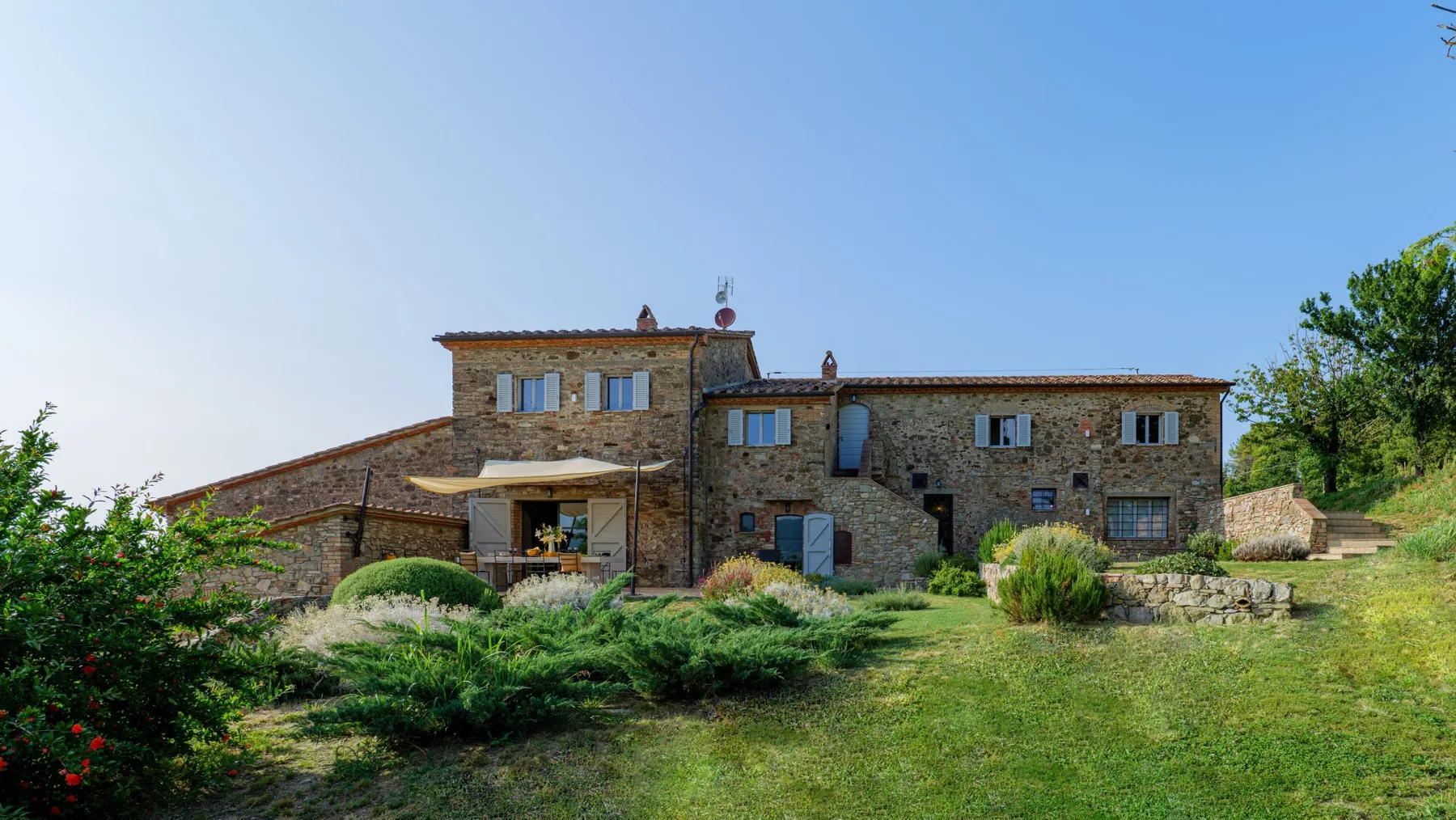 A stone building stands amid landscaped gardens beneath a clear sky.