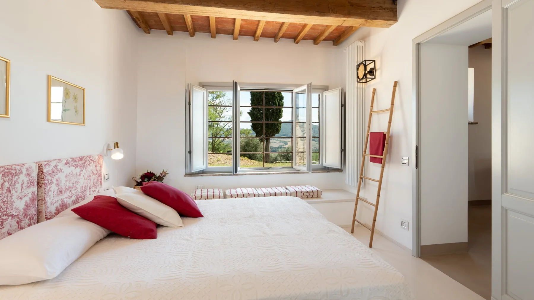 A bright bedroom with a large bed facing open windows overlooking greenery.