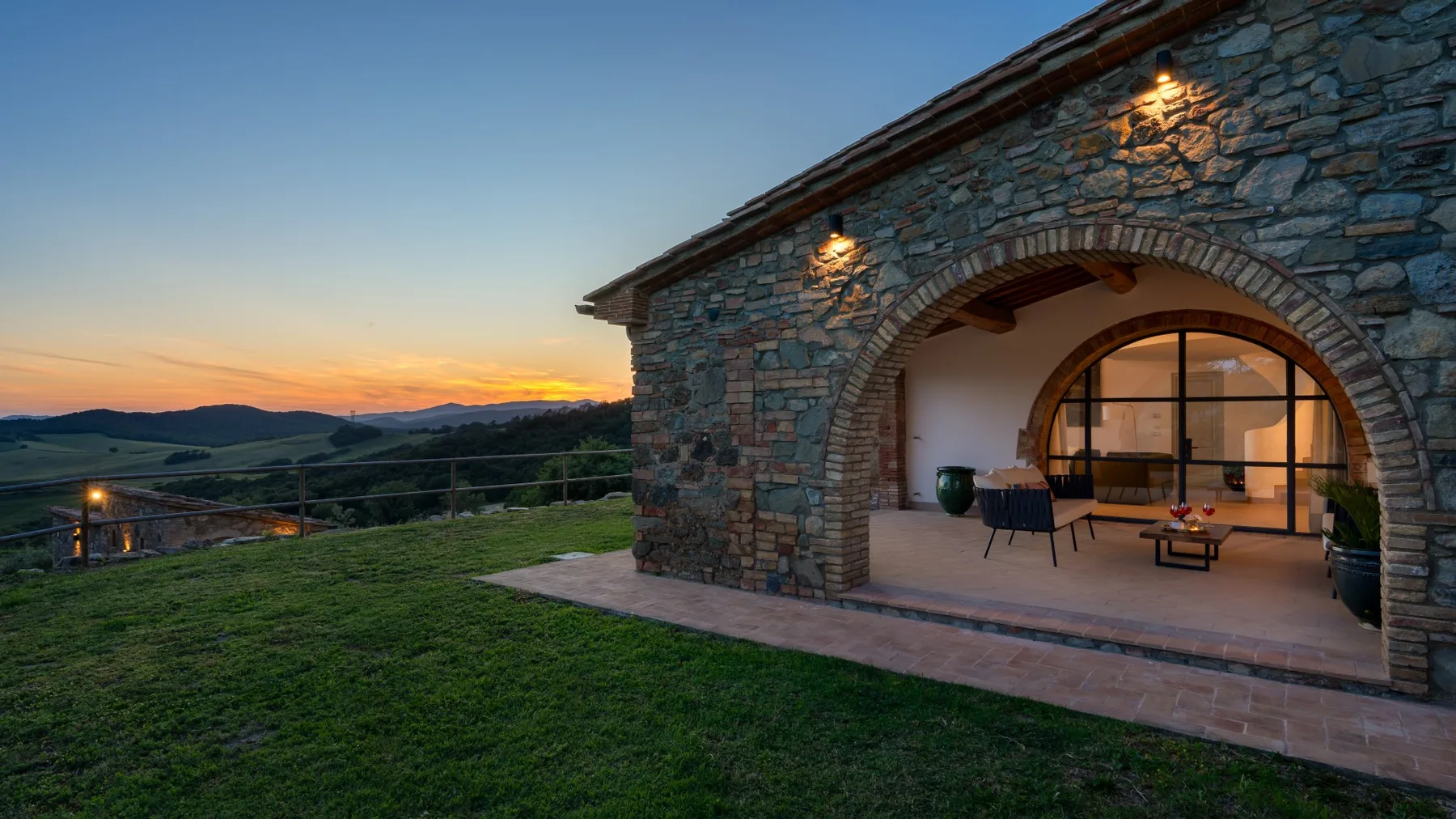 A stone patio with seating overlooks rolling hills at sunset.