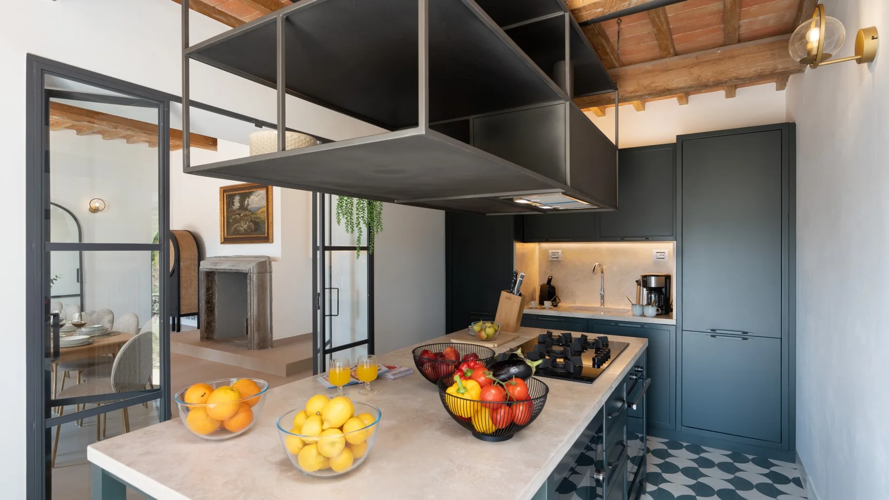 A modern kitchen with a central island, fruit bowls, and dark cabinetry.