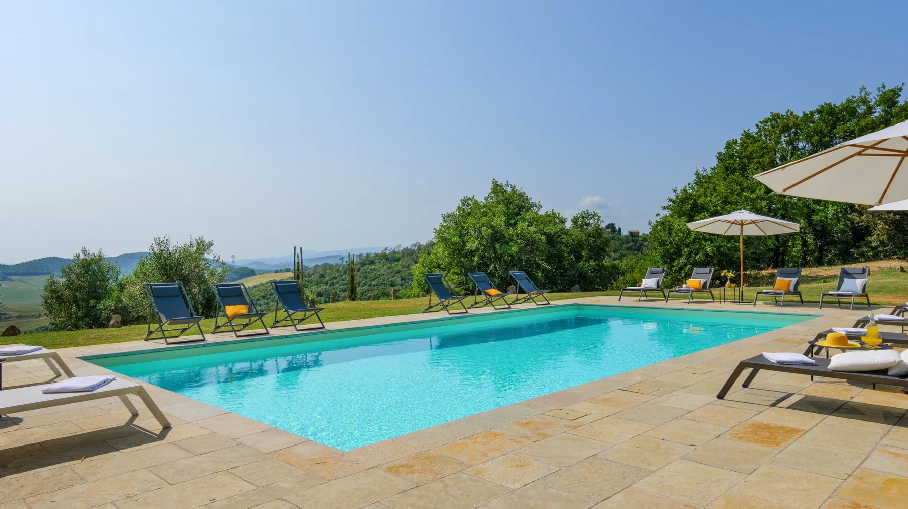 An outdoor swimming pool surrounded by a paved deck and lounge seating.