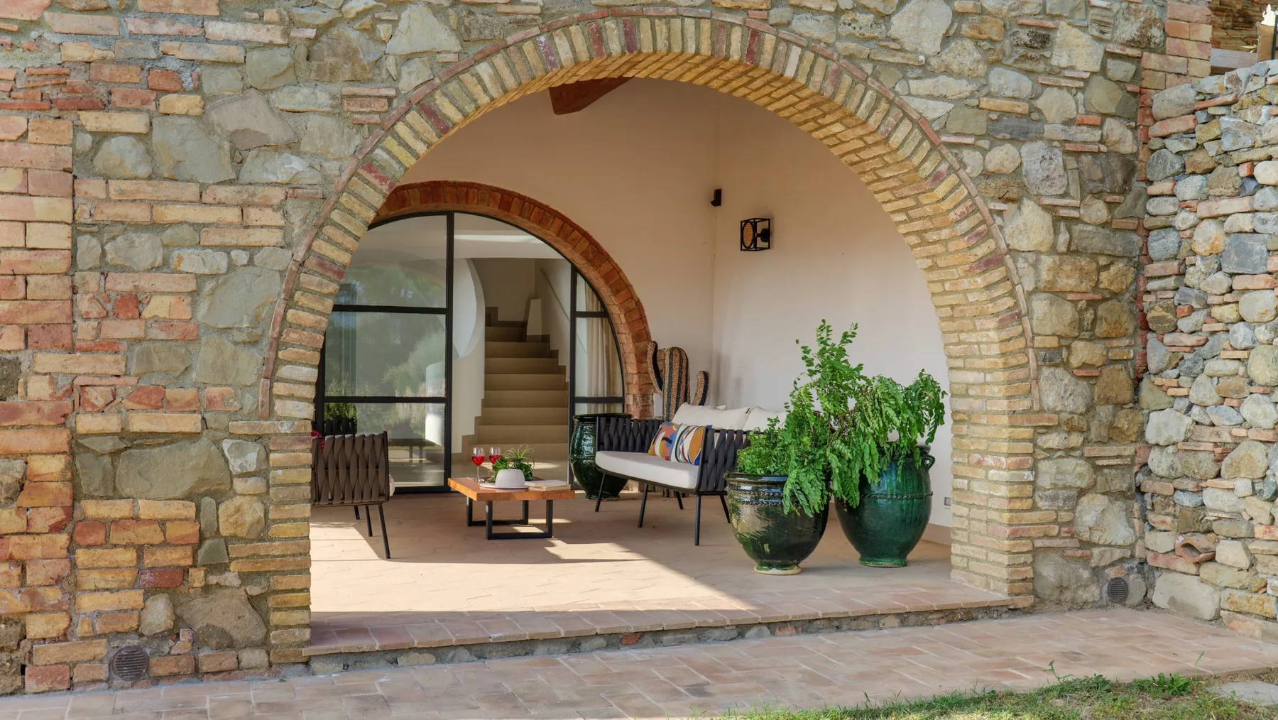 A stone-arched patio with seating and potted greenery.