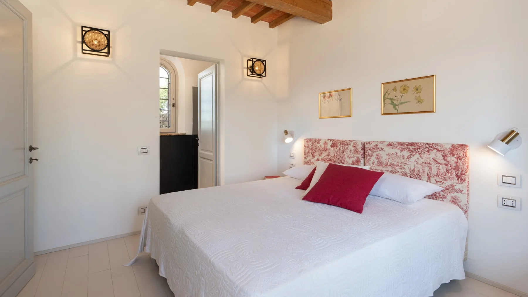 Bedroom with a large bed, red accent pillows, and framed floral artwork.