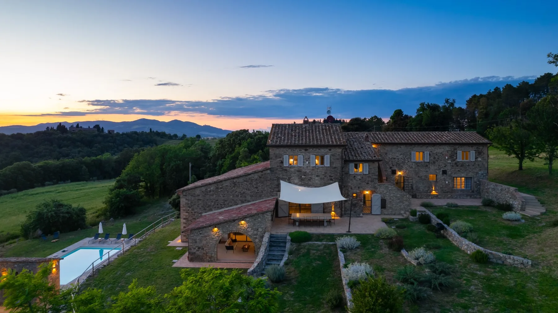 A stone country house stands among green hills beneath a colorful evening sky.