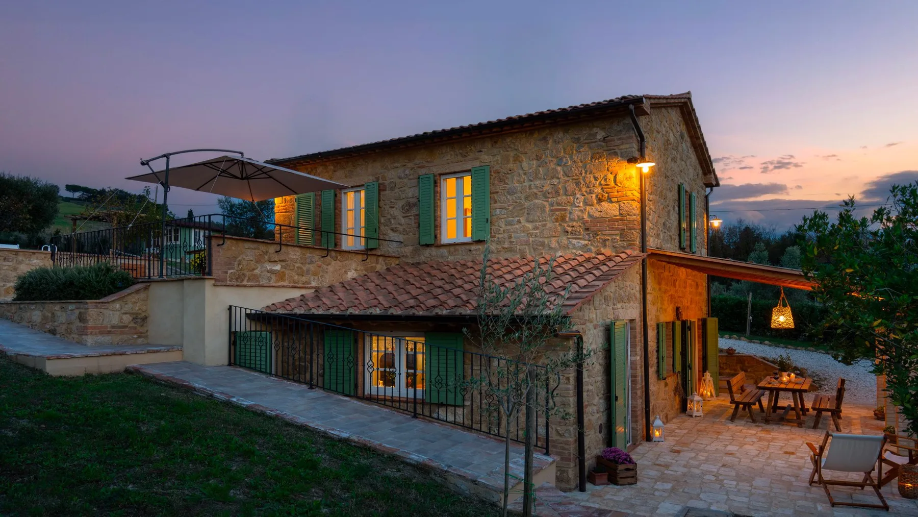 Una casa de piedra con un patio iluminado y asientos al aire libre al anochecer.
