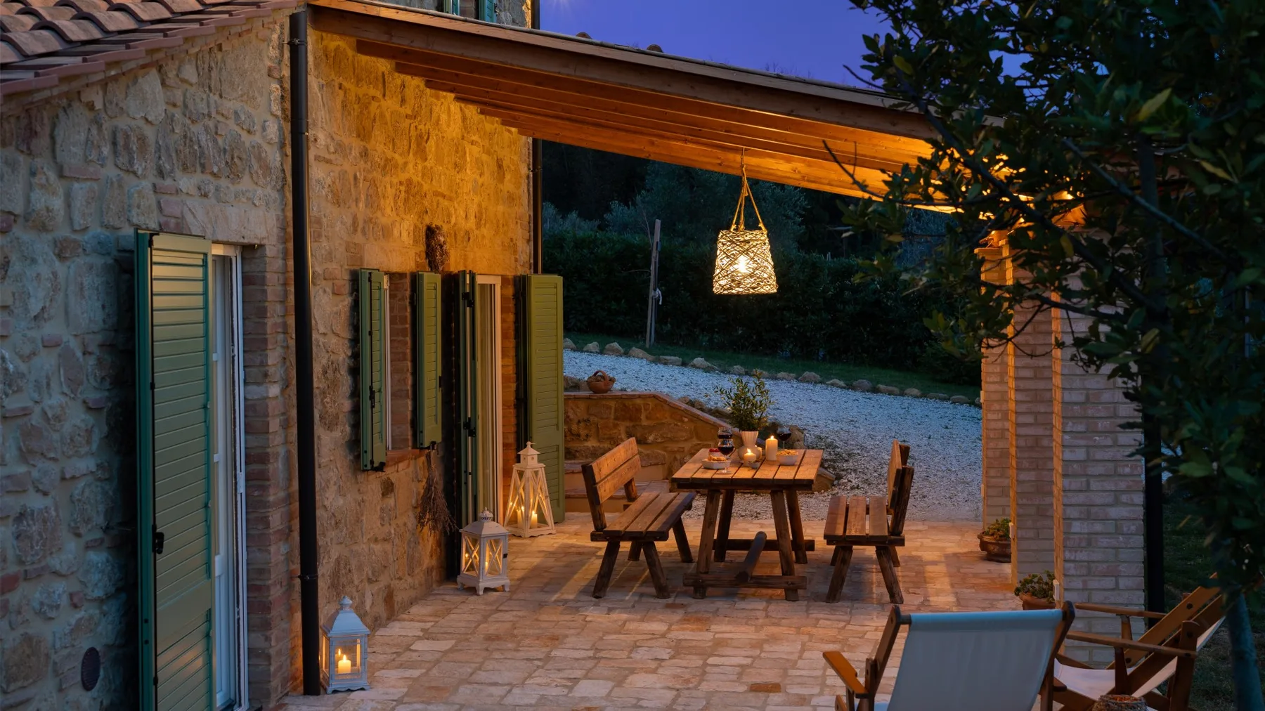 Un comedor en un patio de piedra con mesa y sillas de madera bajo un techo cubierto.