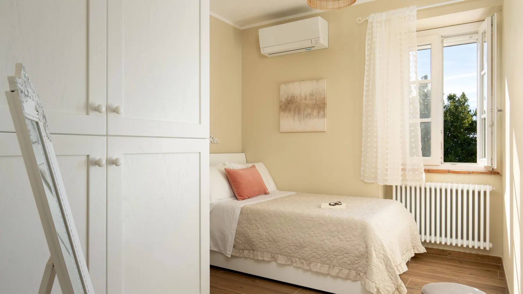 Un dormitorio luminoso con una cama junto a una ventana y un armario blanco.