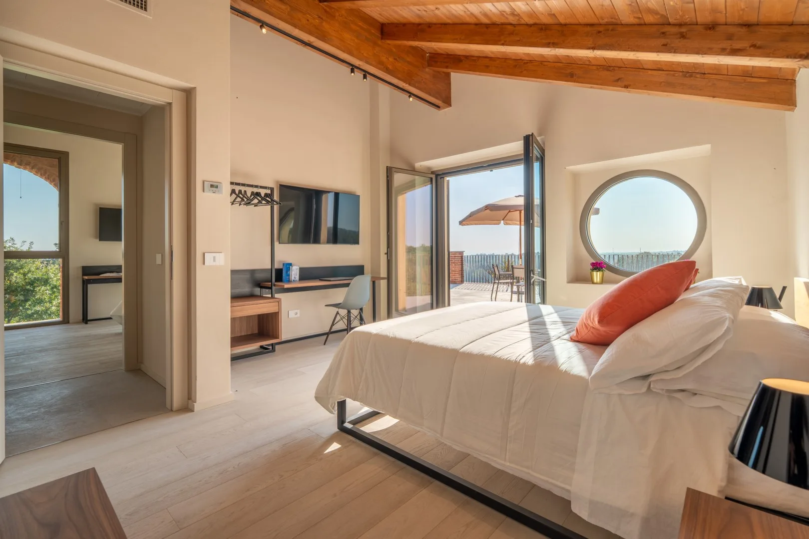 A bright bedroom with a bed, an open glass door, and a round window.