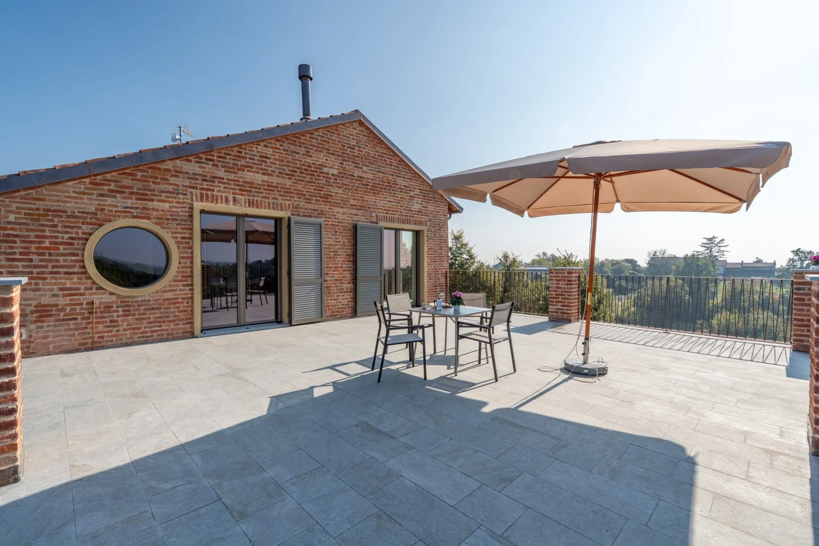 A paved terrace beside a brick building has outdoor seating and a large umbrella.