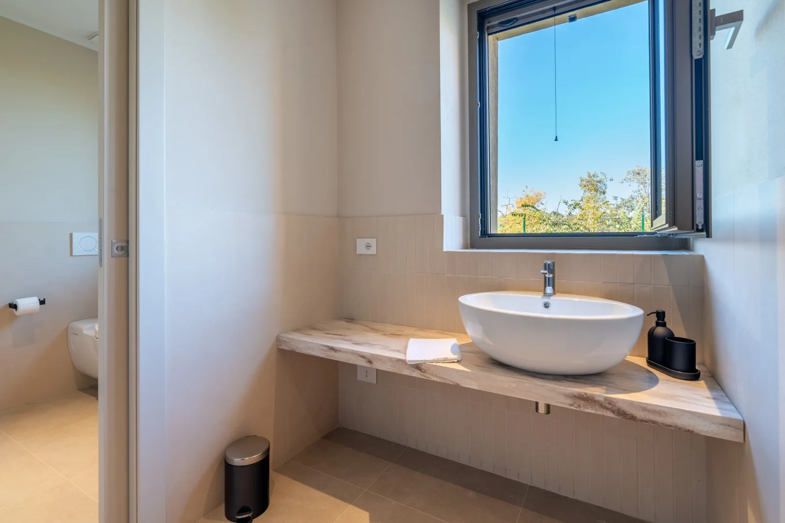 A bright bathroom with a wide sink counter beneath an open window.