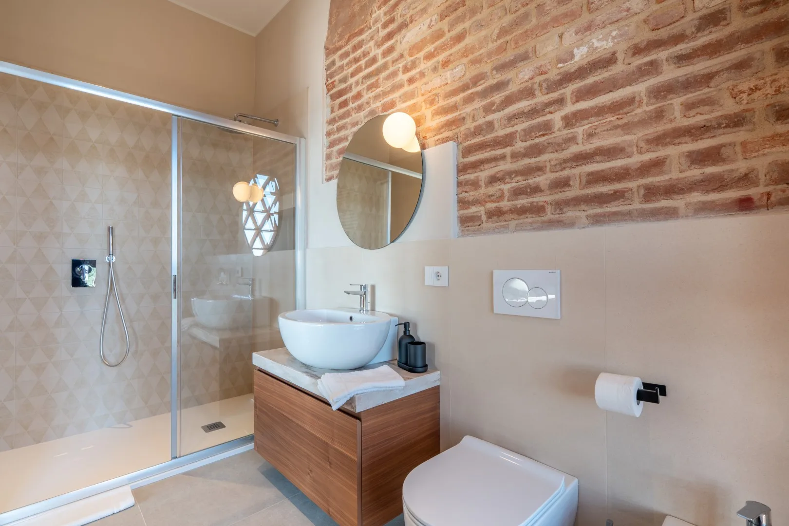 A bathroom with a glass shower, sink, and exposed brick wall.