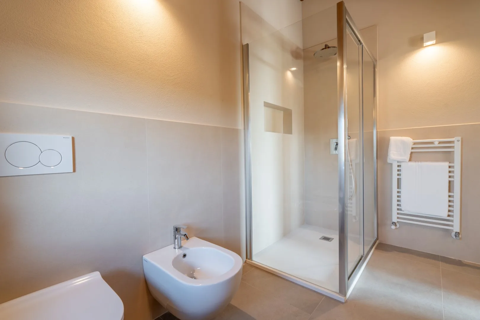 A bright bathroom with a glass shower and a wall-mounted towel warmer.