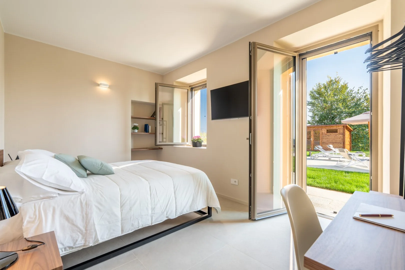 A bright bedroom with a bed and open doors overlooking a garden.