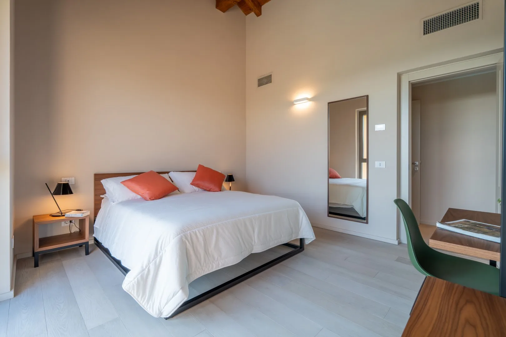 A bedroom with a neatly made bed, bedside table, and desk.