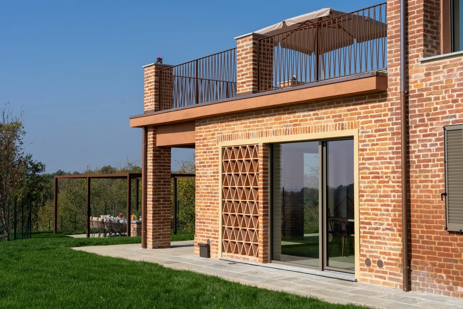 A brick house opens onto a lawn, with a glass door beneath an upper terrace.