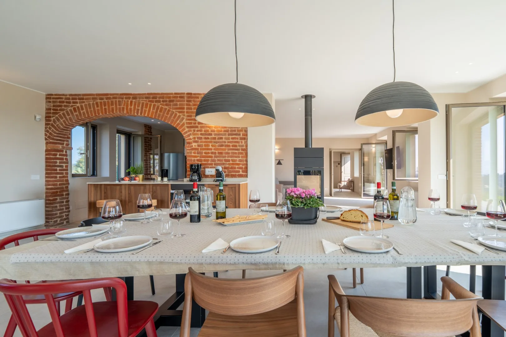 A dining table set with plates sits beneath pendant lights in an open kitchen.
