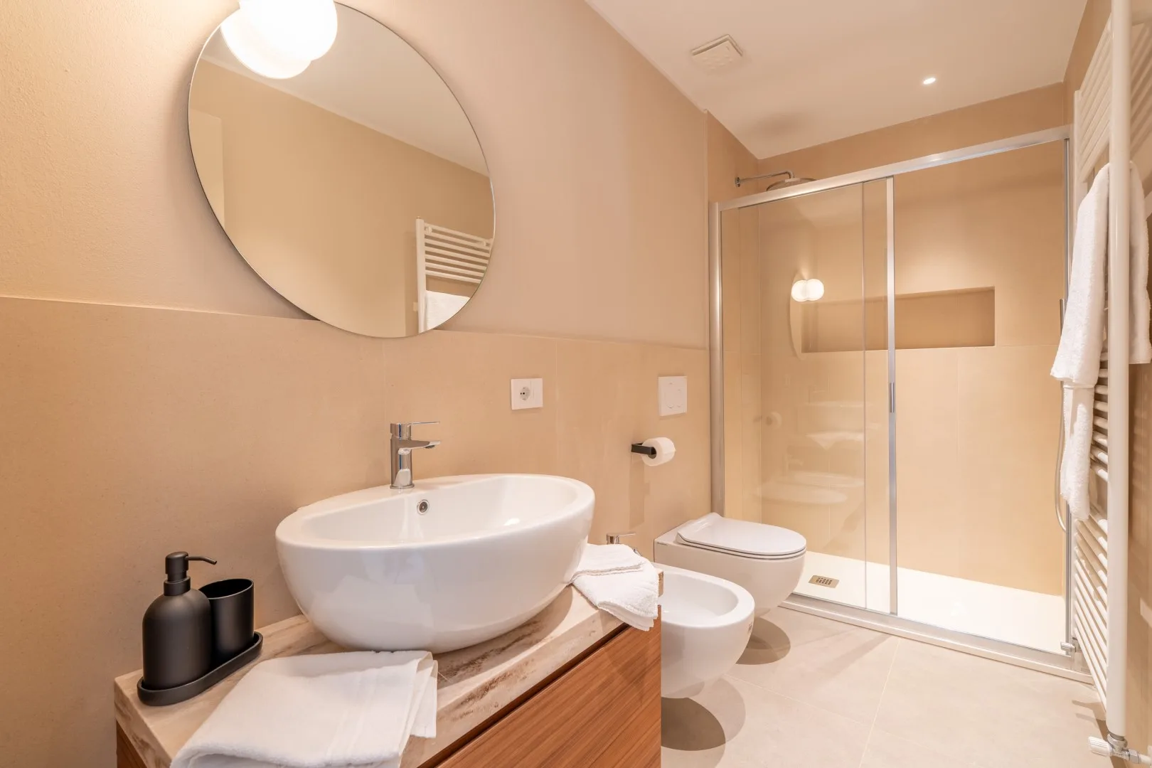 A bathroom with a vessel sink, round mirror, and glass shower.