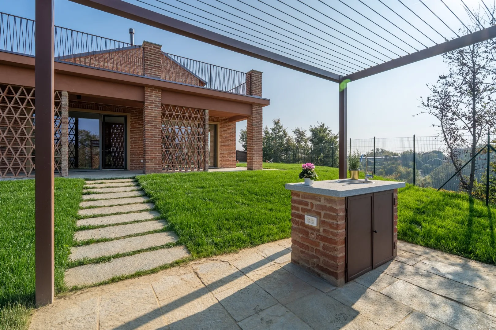 A brick patio and pergola overlook a grassy yard, with a path leading to the house.