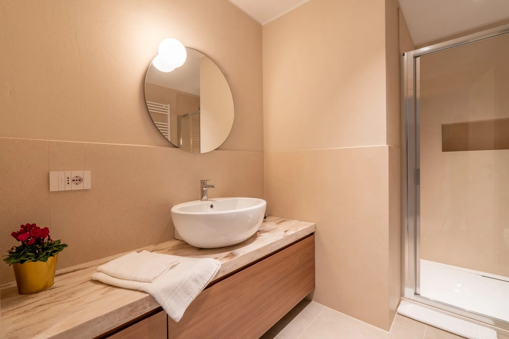 A bathroom vanity with a round mirror and a shower enclosure.