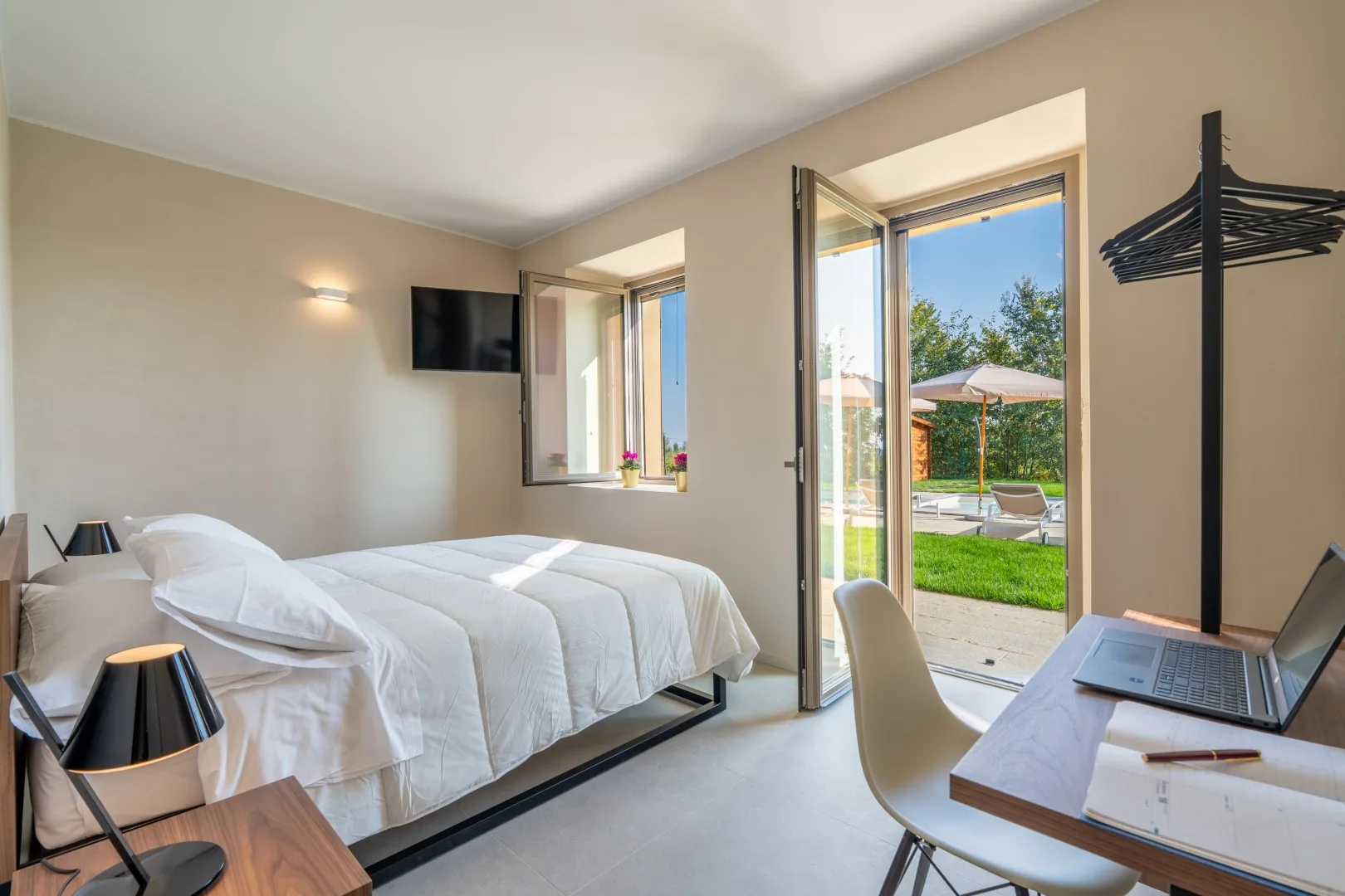 A bright bedroom with a neatly made bed and a glass door opening to a garden.