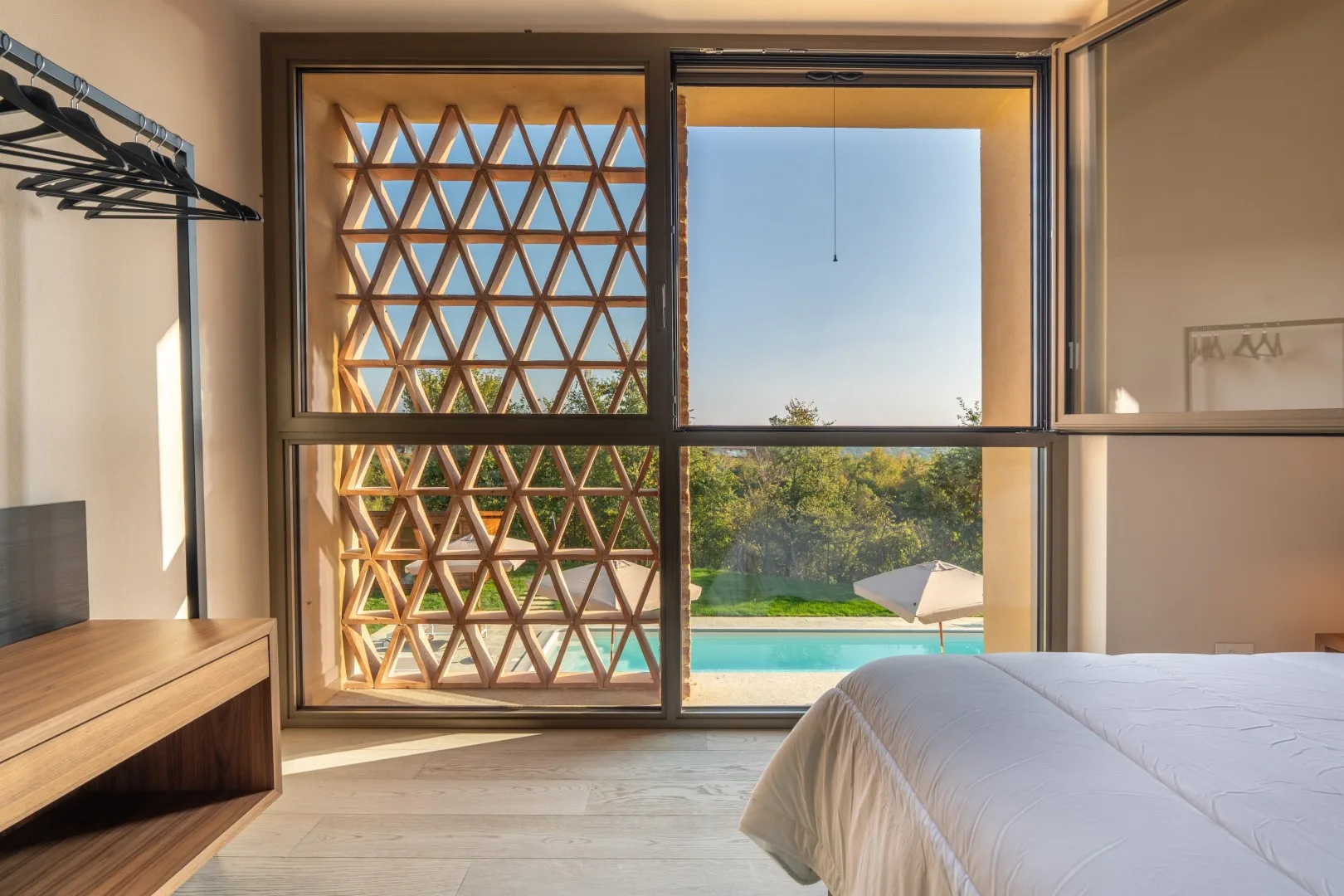 A bedroom with a large window overlooking greenery and a pool.