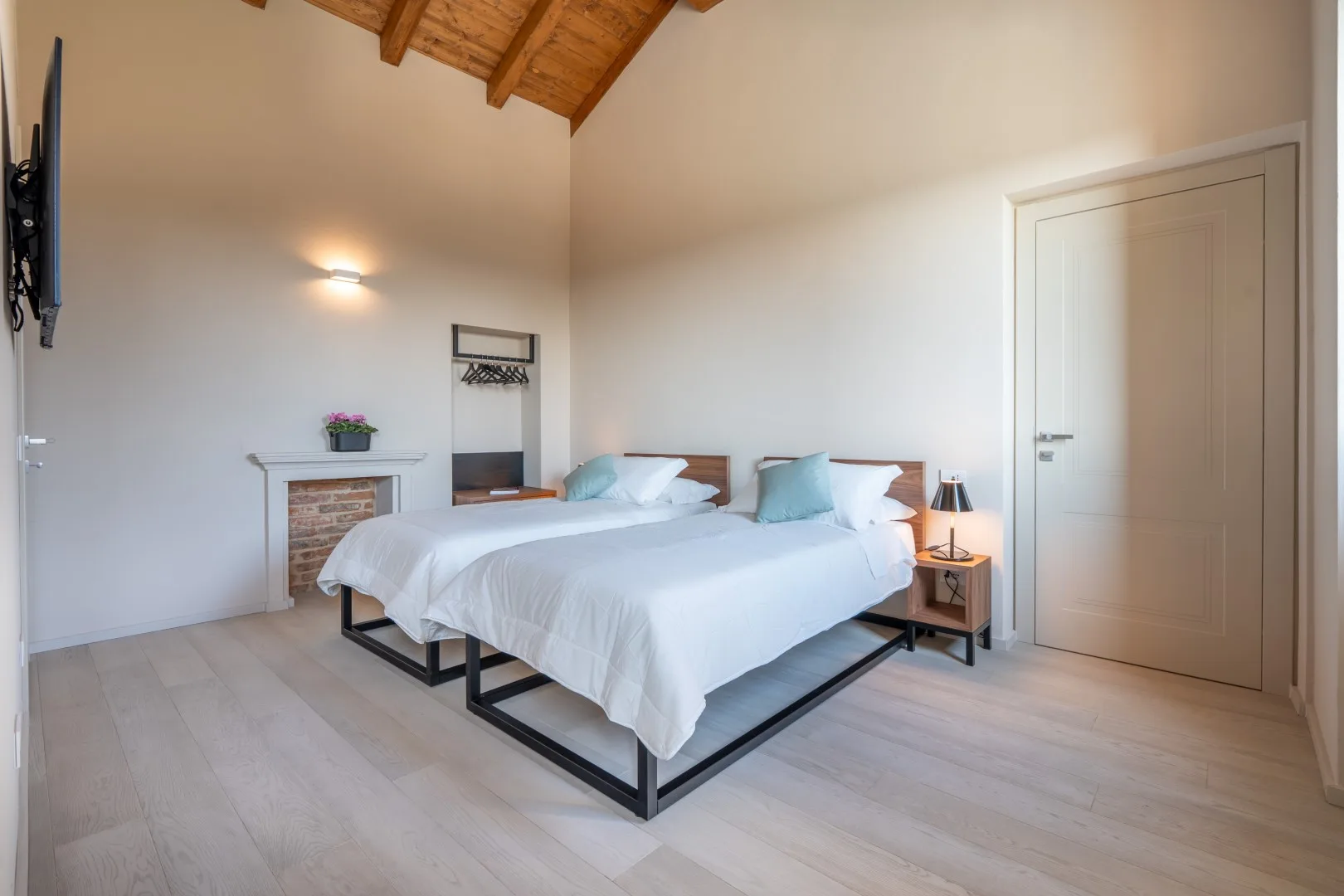 A bright bedroom with two beds beneath a sloped wooden ceiling.