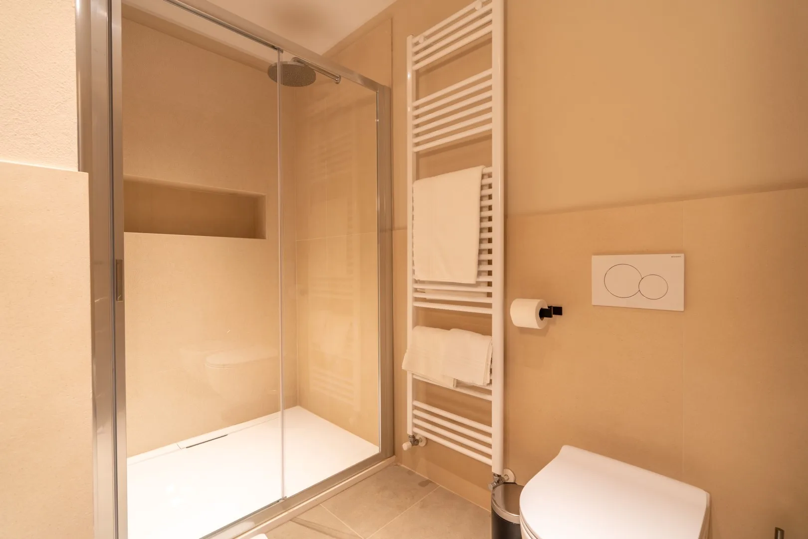 A bathroom with a glass shower, towel warmer, and toilet.