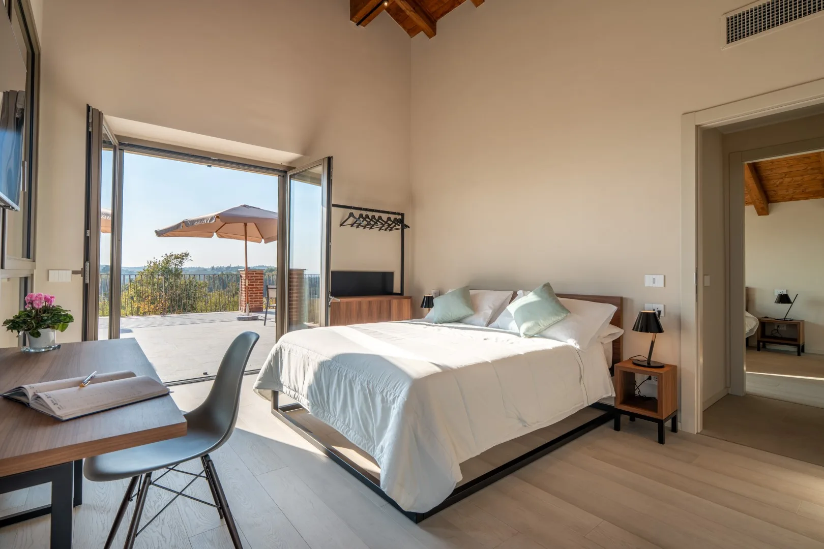 A bright bedroom with a bed and open glass doors leading to a patio.