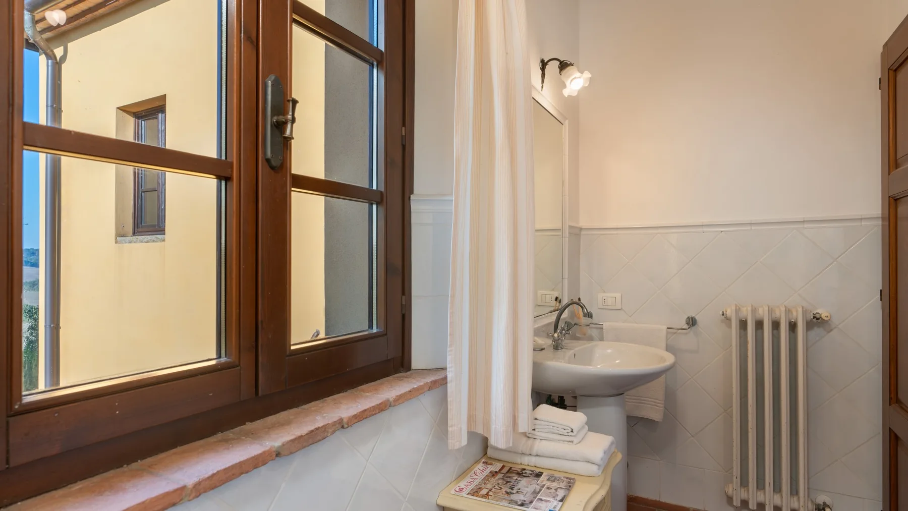 Un baño con lavabo, radiador y zona de ducha con cortina.