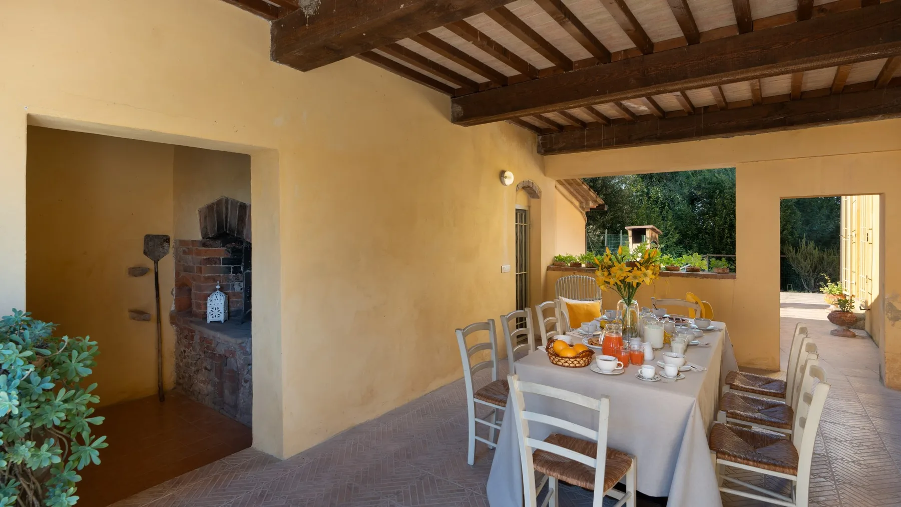 Un comedor exterior cubierto con una mesa larga puesta junto al jardín.