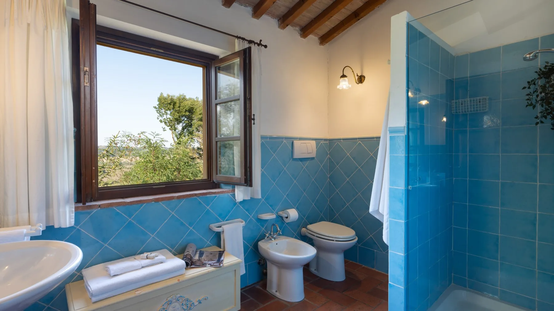 Un baño con paredes de azulejos azules, una ventana y una ducha.