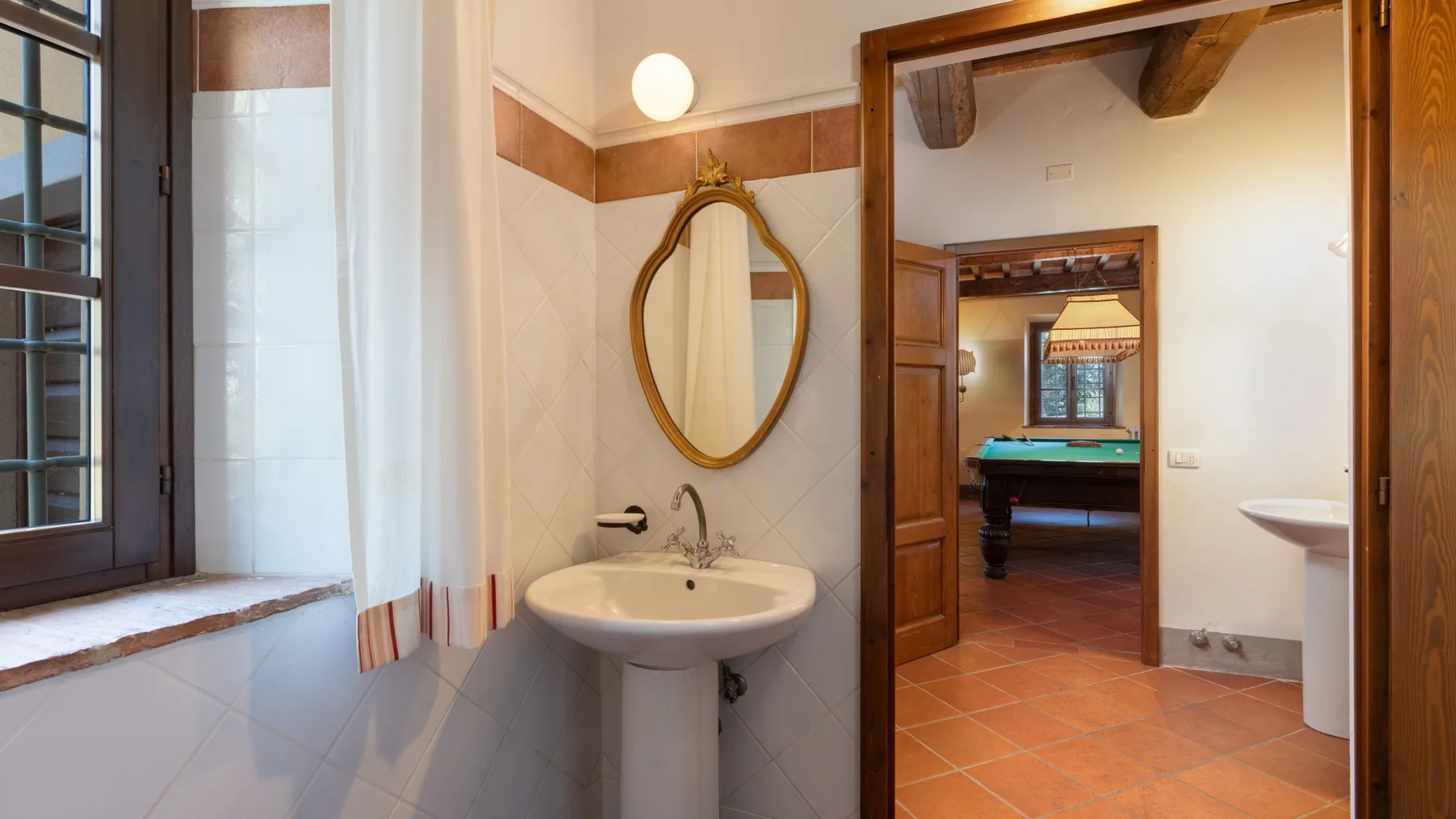 Un baño con lavabo de pedestal y vista a una habitación contigua.