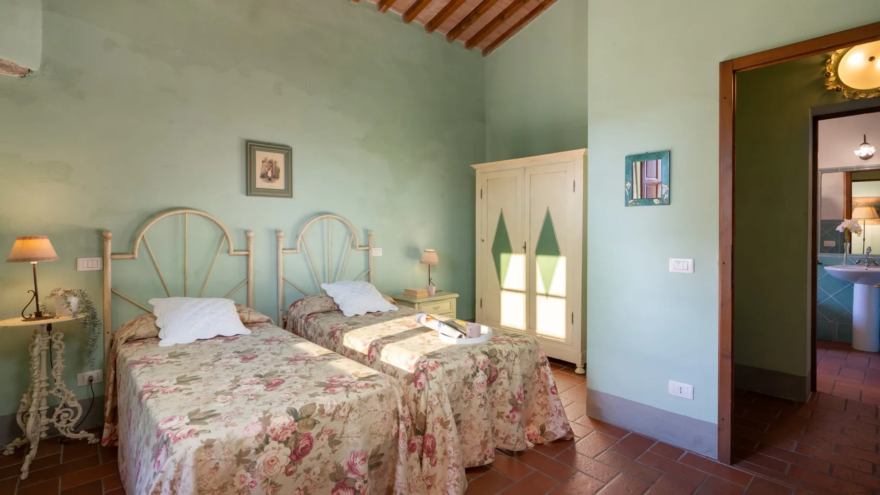 Un dormitorio con dos camas, ropa de cama floral y una pared verde claro.