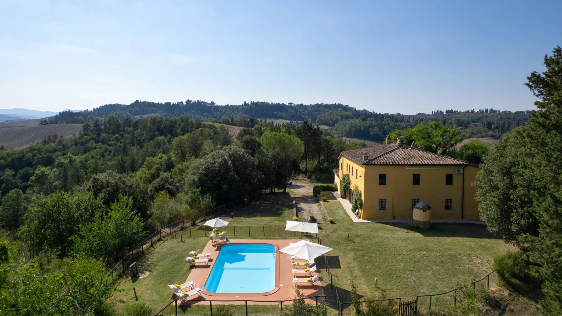 Una casa amarilla está junto a una piscina en un paisaje verde y arbolado.