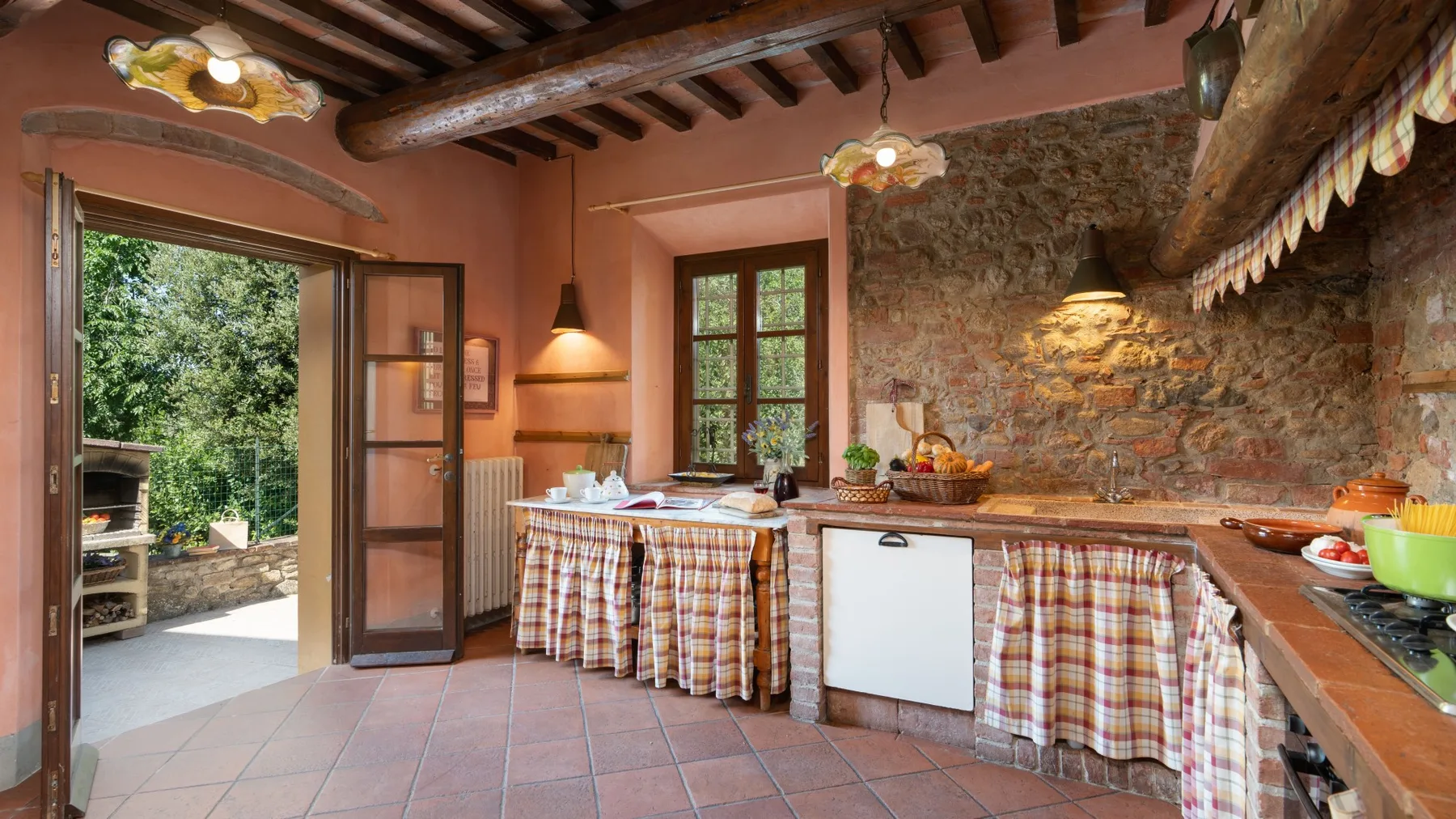 Una cocina rústica con una pared de piedra y una mesa central cubierta con tela a cuadros.