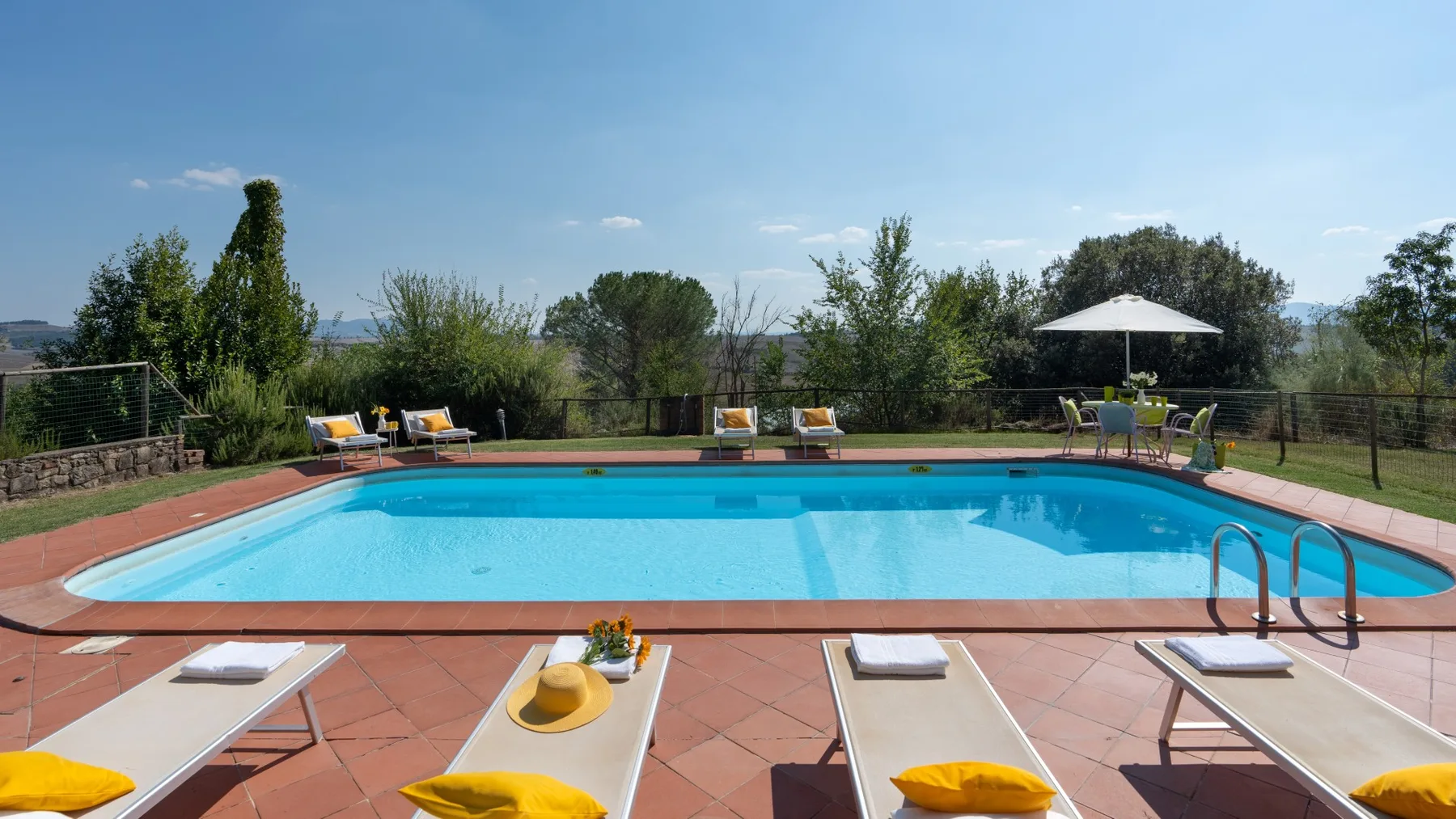 Una piscina al aire libre está rodeada de tumbonas y una terraza.