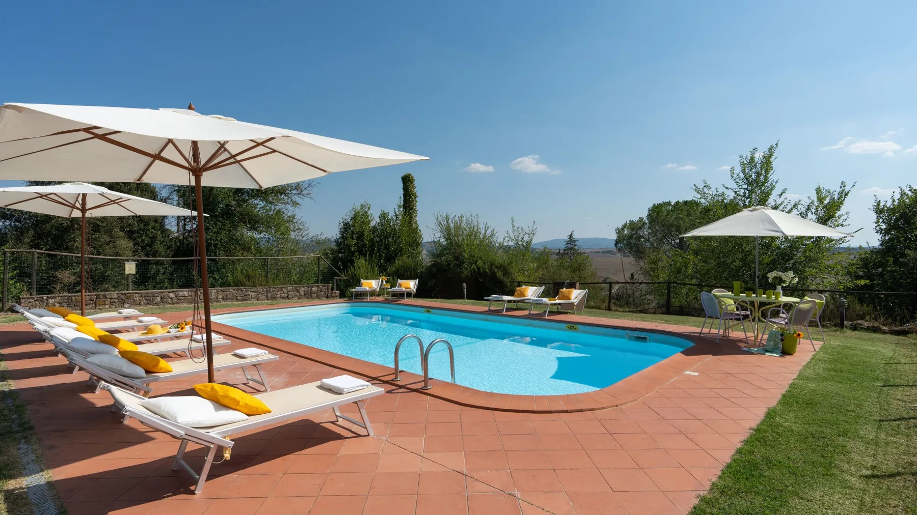 Una piscina al aire libre está rodeada por una terraza pavimentada, tumbonas y sombrillas.