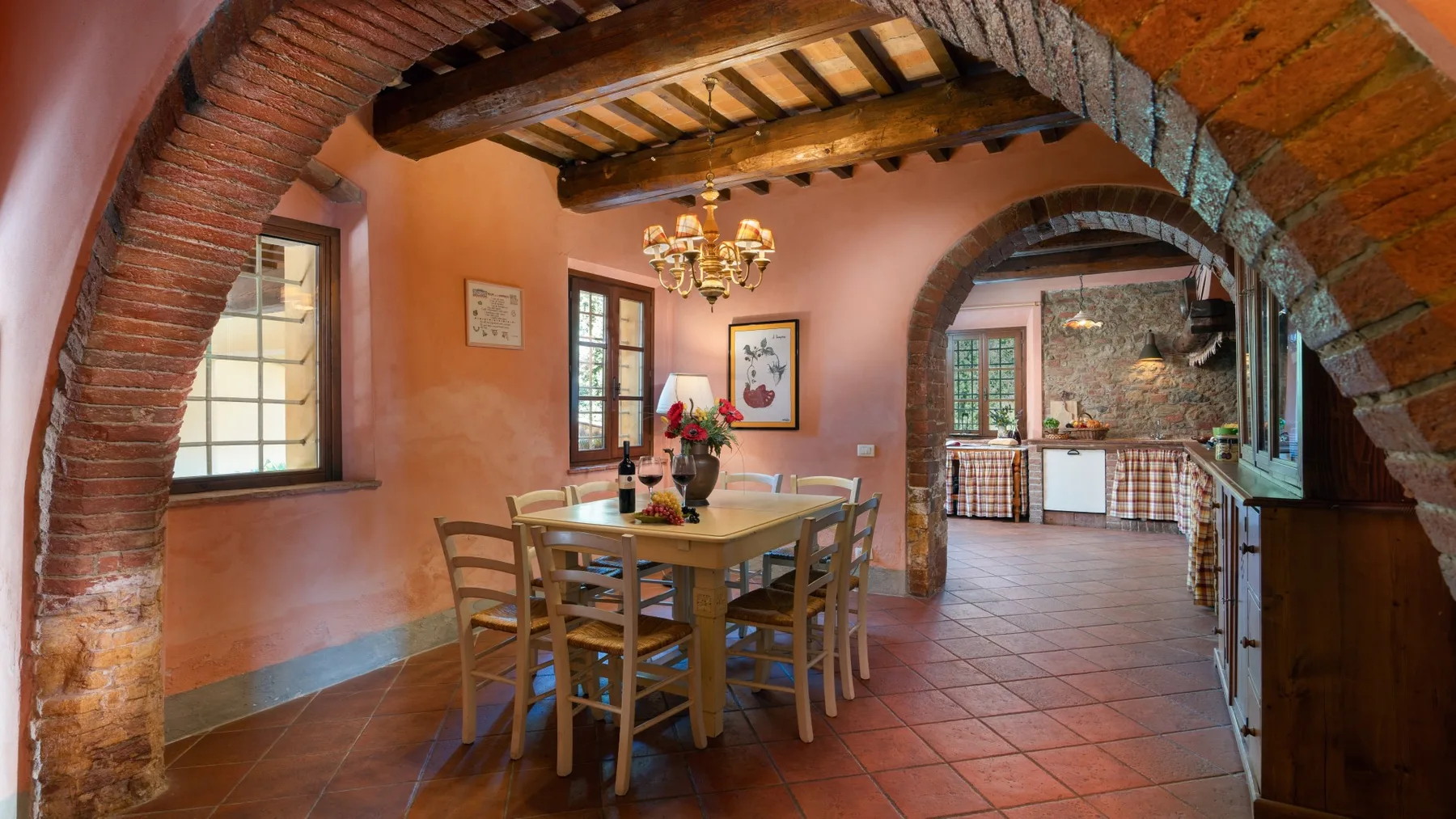 Un comedor con una mesa de madera bajo vigas vistas, abierto a una cocina.